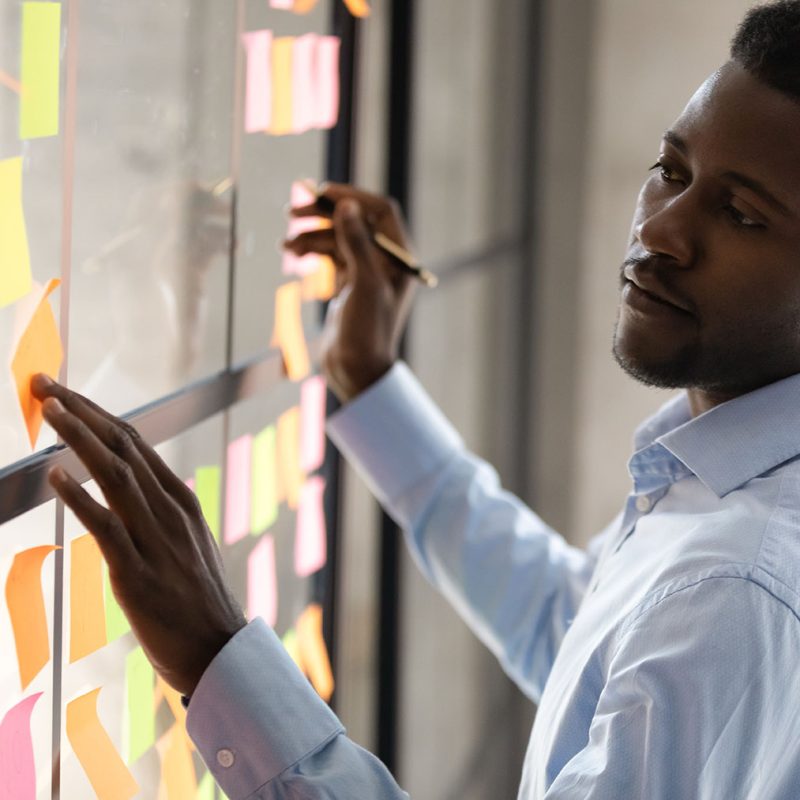 man maps a process using a swim lane on glass with sticky notes